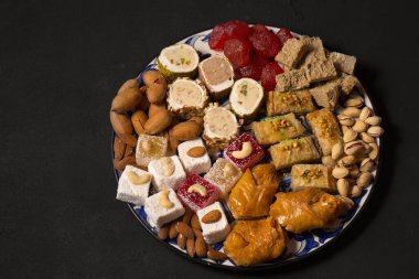 A large plate of various oriental sweets and nuts on a dark background
