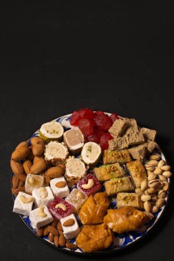 A large plate of various oriental sweets and nuts on a dark background