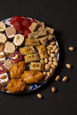 A large plate of various oriental sweets and nuts on a dark background