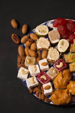 A large plate of various oriental sweets and nuts on a dark background