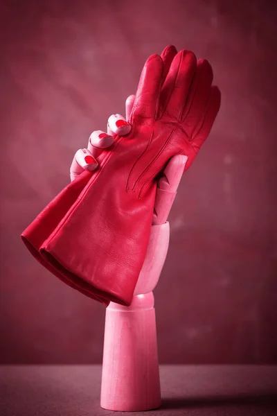 Beautiful pink gloves in wooden hand, on gray background