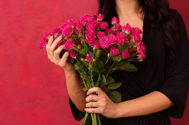 A young woman in a black dressing gown with a deep neckline holds a bouquet of pink roses, on a pink background, close-up, on a pink background.