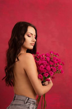 A beautiful young woman is holding a bouquet of pink roses on a pink background.