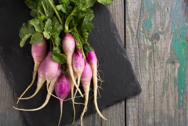 Taze bahar turpu, mor-beyaz ten ve ahşap bir tahtada otlar.