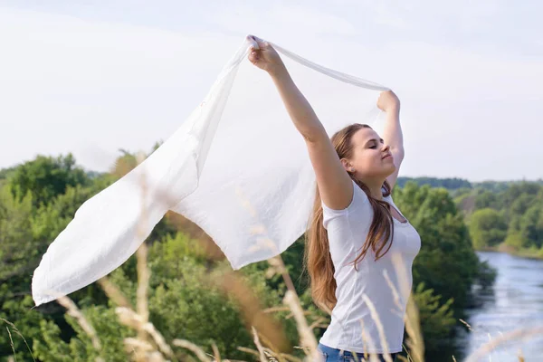 一个手里拿着白布的快乐的年轻女子在大自然中迎风而行 — 图库照片