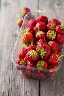 Tahta bir arka planda plastik bir kapta sulu, olgun kırmızı çilek.