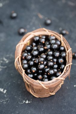 Koyu bir masada, ahşap bir sepetin içinde olgun siyah üzümler.