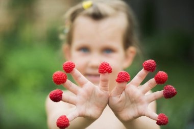 Küçük neşeli bir kız bahçede parmağına ahududu takmış.