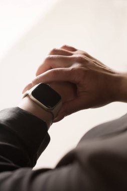 Genç ofis çalışanı akıllı saate bakıyor, elleri yakın.