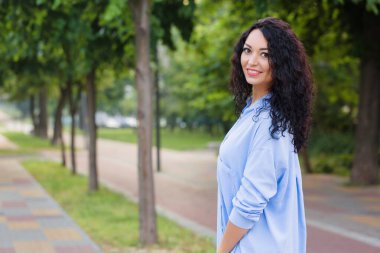 Mavi uzun gömlekli, gülümseyen güzel bir iş kadını sokakta yürüyor.