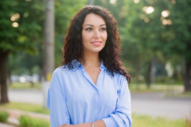 Mavi uzun gömlekli, gülümseyen güzel bir iş kadını sokakta yürüyor.