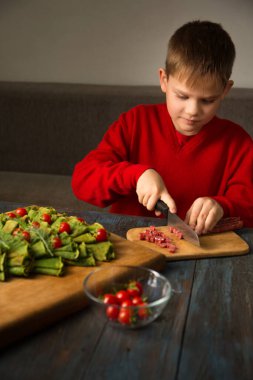 Tahta bir tahtanın üzerinde noel ağacı şeklinde ıspanaklı krep. Küçük bir çocuk kiraz domatesli ve sosisli krepten yapılmış bir Noel ağacını süslüyor. Krep tahtası.