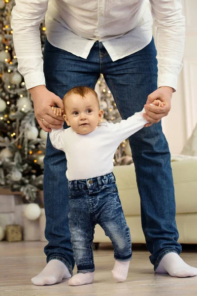 Dad teaches his little child to walk by holding hands near the Christmas tree