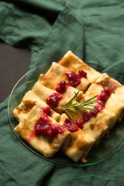 Kızılcık soslu peynirle doldurulmuş krepler, karanlık bir arka planda kış tatlısı.