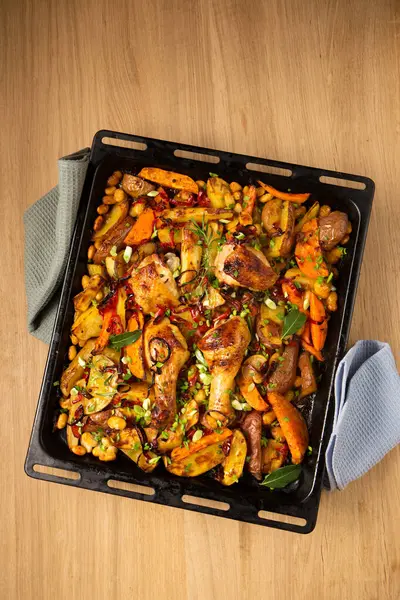 Baked vegetables with ruddy baked chicken on a large metal tray on a wooden table