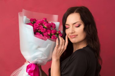 Pembe arka planda küçük pembe güllerle dolu buketi olan güzel, siyah saçlı bir kadın.