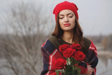 Kırmızı şapkalı ve battaniyeli genç bir kadın ve bir buket kırmızı gül. Sevgililer Günü konsepti
