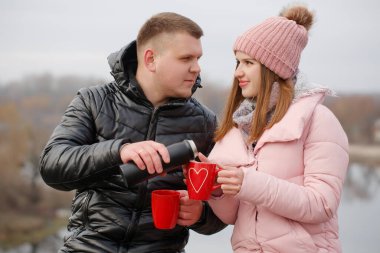 Genç çift nehir kenarında sıcak bir şeyler içiyor. Sevgililer Günü konsepti