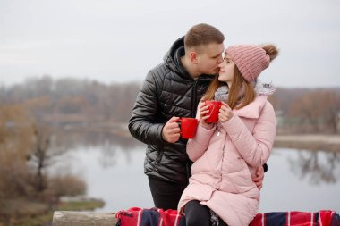 Genç çift nehir kenarında sıcak bir şeyler içiyor. Sevgililer Günü konsepti