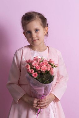 Pembe elbiseli şirin küçük bir kız pembe arka planda pembe güller tutuyor.