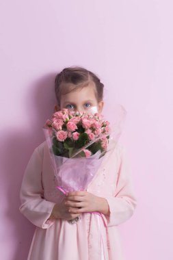 Pembe elbiseli şirin küçük bir kız pembe arka planda pembe güller tutuyor.