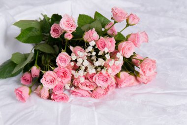 Güzel bir buket pembe gül beyaz bir kumaşın üzerinde yatıyor.
