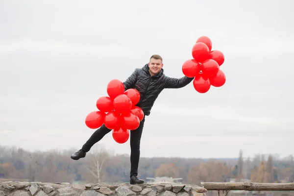Young cheerful man with red balloons, outdoors. Valentine\'s day concept