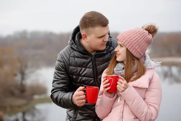 Young couple drinking a hot drink outside by the river. Valentine\'s day concept