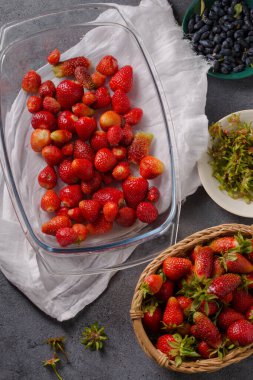 Sepette sulu olgun çilekler ve gri arka planda şeffaf bir tabak.