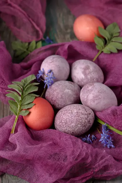Still life of beautiful textured purple eggs on purple gauze with spring flowers