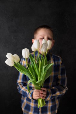 Çocuk elinde siyah arka planda beyaz laleler tutuyor.