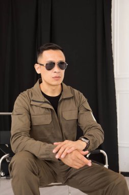 Stüdyoda bir sandalyede oturan güneş gözlüklü bir adamın portresi.