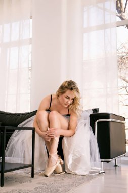 Tutu etekli bir balerin, vahşi bir deri koltukta otururken sivri ayakkabılar giyer.