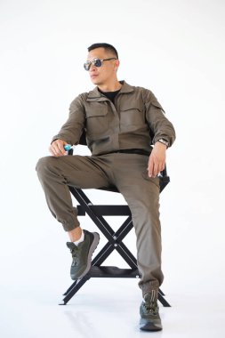 Elektronik sigaralı güneş gözlüklü bir adam beyaz arka planda bir sandalyeye oturur.