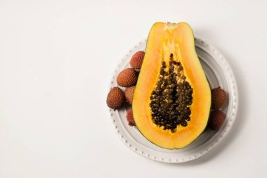 Beyaz bir masada beyaz bir tabakta sulu, olgun bir papaya 'nın yarısı.