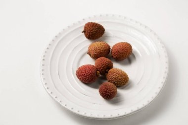 Beyaz bir masada beyaz bir tabakta taze tropikal liçi üzümü.