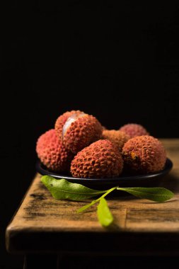 Masanın kenarında, siyah bir arka planda, siyah bir tabakta küçük, olgun tropikal liçi üzümleri.