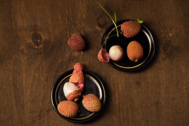 Masanın kenarındaki siyah bir tabakta, ahşap bir arka planda, küçük olgun tropikal liçi üzümleri.