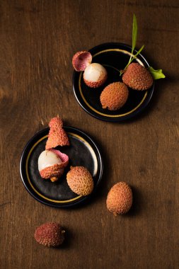 Masanın kenarındaki siyah bir tabakta, ahşap bir arka planda, küçük olgun tropikal liçi üzümleri.