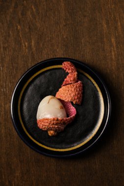 Masanın kenarında, ahşap bir arka planda, siyah bir tabakta küçük olgun tropikal liçi üzümleri.