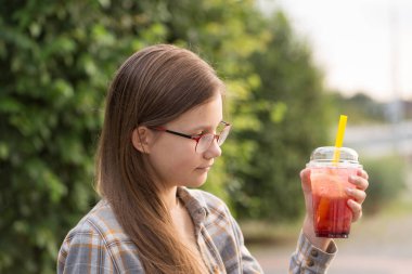 Gözlüklü genç bir kız şehirde yürürken köpüklü çay içer.