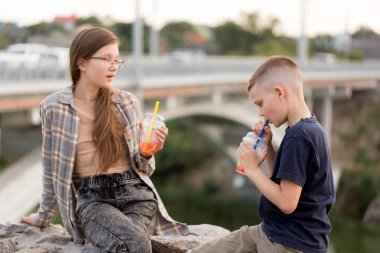 İki çocuk akşam yürürken plastik bardaklardan köpüklü çay içer.