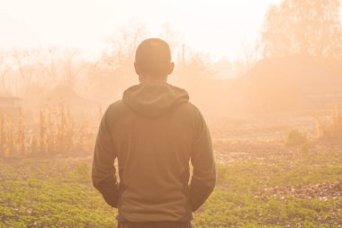 Kırsalda sisli bir sonbahar sabahının tadını çıkaran bir adamın arka portresi.