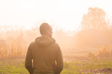 Kırsalda sisli bir sonbahar sabahının tadını çıkaran bir adamın arka portresi.