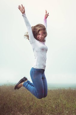 Genç bir kadın, sonbahar sisli tarlasında Holi boyalarıyla kaplı olarak yükseğe zıplıyor.