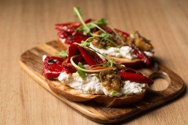 Peynirli sandviçler, mantarlar, ızgara biber ve ahşap bir tahtanın üzerinde mikro yeşil bezelye kabukları.