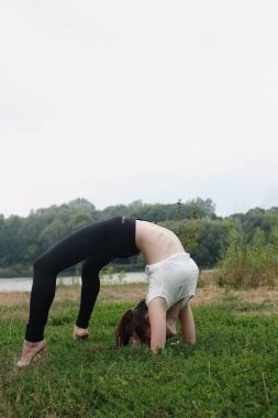Kadın nehir kenarındaki eğitim alanında amuda kalkıyor. Özgürlük ve güç kavramı, kadın yoga pozisyonunda olduğu için. Alanın doğal yapısı genel olarak barışçıl.