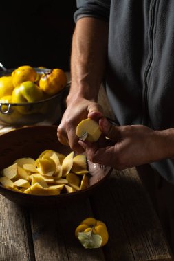 Adamın biri, eski bir ahşap masada, bir kasede sarı ayva meyvesi kesiyor. Fotoğraf kırsal stilde