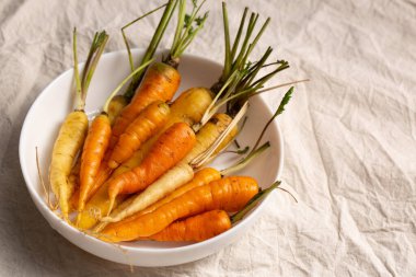 Beyaz, sarı ve turuncu havuçlar beyaz bir kasede, masa örtüsünün üzerinde. Çeşitli sebze konsepti