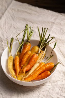 Beyaz, sarı ve turuncu havuçlar beyaz bir kasede, masa örtüsünün üzerinde. Çeşitli sebze konsepti